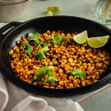 Blackened corn with homemade seasoning served in a skillet with lime wedges and cilantro.