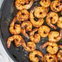 Blackened shrimp with homemade seasoning in a black skillet with butter.