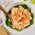 Buffalo chicken salad with fresh spinach, a whole wheat wrap, and a spoon in a bowl.