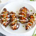 Buffalo chickpea stuffed sweet potatoes on a plate drizzled with ranch dressing and green onions.