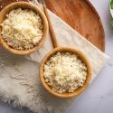 Cauliflower rice made with fresh cauliflower florets in two wooden bowls with fresh herbs on the side.