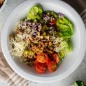 Cheeseburger salad with ground beef, pickles, tomatoes, lettuce, and shredded cheddar cheese in a bowl.