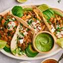 Chicken carnitas tacos with fresh cilantro, diced white onion, avocado, and salsa verde in corn tortillas.