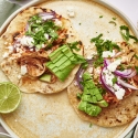 Chicken tinga tacos served on corn tortillas with queso fresco, cilantro, lime, and red onion.