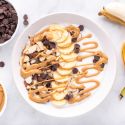 Chunky monkey banana peanut butter Greek yogurt bowl with sliced bananas, almonds, chocolate chips, and melted peanut butter.