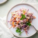 Coleslaw with shredded purple cabbage, green cabbage, carrots, and cilantro on a white plate.