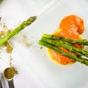 Crispy polenta with asparagus in a creamy tomato sauce on a clear plate with herbs.