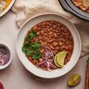 Crockpot pinto beans in a bowl with red onions, cilantro, and lime slices. 