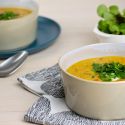 Slow cooker red lentil soup with curry powder and carrots in a bowl with herbs and yogurt.