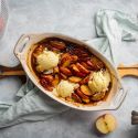 Baked apples in a ceramic baking dish with vanilla ice cream and cinnamon.