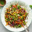 Edamame salad with shelled edamame, kale, carrots, red bell peppers, peanuts, cilantro, and mint served with peanut dressing.