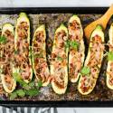 Fajita stuffed zucchini with pinto beans on a baking sheet with beans, peppers, onions, and melted cheese.