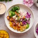 Fish taco bowls with flaky mahi mahi, avocado, mango, limes, shredded cabbage, cilantro, and taco sauce in a bowl with rice.