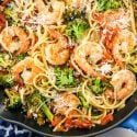 Garlic lemon and shrimp and broccoli pasta in a pan with fresh lemon slices and Parmesan cheese.