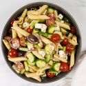 Greek pasta salad with tomatoes, cucumbers, black olives, feta cheese, and Greek dressing in a bowl. 