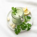 Green goddess dressing in a glass jar with fresh cilantro, garlic, and lemon on the side.