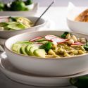 Green pozole with shredded chicken, hominy, cilantro, and avocado in a bowl.