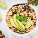 Green turkey chili with ground turkey, black beans, white beans, corn, and sliced avocado in a bowl.