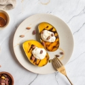 Grilled mango sliced in half on a plate with a dollop of yogurt, honey, and pistachios.