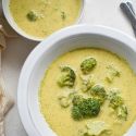 Healthy Broccoli Cheese Soup with broccoli florets, cheddar cheese, and a creamy broth in two bowls.