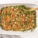 Healthy Green Bean Casserole with green beans, mushroom sauce, and a crispy almond onion topping in a baking dish with a striped napkin.