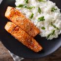 Honey soy salmon with glaze served on a bed of white rice with green onions and sesame seeds.