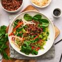 Korean beef bowls with rice, cilantro, carrots, bell peppers, and sprouts in a bowl with spicy sauce. 