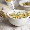 Slow cooker lemon artichoke chicken soup with quinoa in a bowl with carrots and lemon.