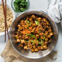 Mongolian tofu in a skillet with carrots, green onions, crispy tofu, and a sweet and spicy sauce.