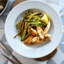 One pan lemon garlic chicken and asparagus served with fresh lemons in a bowl and in a skillet.