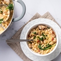 Orzo pasta with chicken breast, spinach, tomatoes, and white beans served in a bowl with Parmesan cheese.