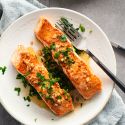 Pan seared salmon with garlic, lemon, and butter served on a plate with a lettuce and tomato salad.