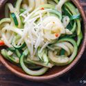 Parmesan zucchini noodles with shredded Parmesan cheese, red pepper flakes, and black pepper in a wooden bowl.