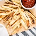 Parsnip fries cut into match sticks with spices on a wooden cutting board with kethcup.