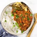 Picadillo with potatoes, carrots, and chipotle tomato sauce in a bowl with rice, tortillas, and cilantro.