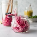 Pickled red onions in a glass jar with lime juice, vinegar, and peppercorns. 