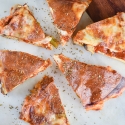 Pizza frittata with tomato sauce and melted cheese cut into slices on a cutting board.