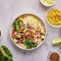 Rice bowl with cooked chicken, black beans, corn, pico de gallo, avocado, and cheese.