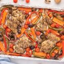 Roasted balsamic chicken thighs with vegetables on a sheet pan sprinkled with Italian seasoning.