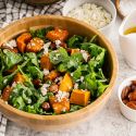 Roasted butternut squash salad with arugula, roasted squash, almonds, feta cheese, and orange vinaigrette in a wooden bowl.