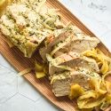 Roasted pork tenderloin and apples with sliced onions cooked and sliced on a wooden cutting board.