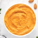 Romesco sauce with blended almonds, tomatoes, and red peppers in a small white bowl with parsley and lemon on the side.