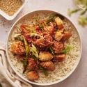 Salmon stir fry with chunks of salmon, asparagus, carrots, and red pepper in a bowl with steamed rice. 