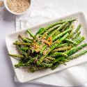 Sesame green beans on a plate with sautéed garlic, sesame seeds, and soy sauce.