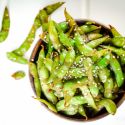 Stir fried edamame in a wooden bowl served with soy sauce and sesame seeds.