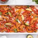 Sheet pan chicken fajitas with chicken breast, peppers, onions, and limes on a baking sheet .