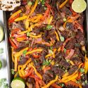 Sheet pan steak fajitas made with homemade fajita seasoning, flank steak, bell peppers, and onions on a sheet pan. 