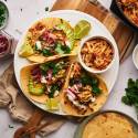 Shredded chicken tacos with avocado, pickled onions, cilantro, and limes on a plate.