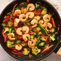 Shrimp stir fry with broccoli, snap peas, peppers, onions, and carrots in a skillet with stir fry sauce.