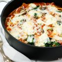 Stovetop lasagna with mushrooms, spinach, melted cheese, and marinara sauce in a skillet.